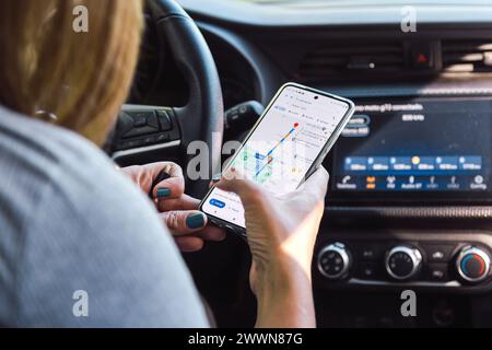 Frau im Auto, die Google Maps auf ihrem Handy benutzt. Suchen einer Route in der GPS-App. ROSARIO, ARGENTINIEN - 22. MÄRZ 2024. Stockfoto