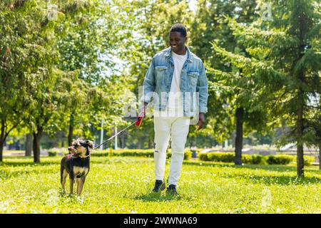ein lateinamerikanischer Mann läuft mit seinem süßen Hund an einem sonnigen Tag im Stadtpark auf dem Rasen Stockfoto