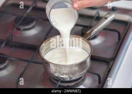 Koche Milch in einem kleinen Topf auf dem Herd. Milchbrei zubereiten. Stockfoto