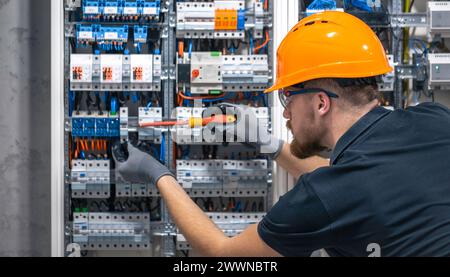 Ein Elektriker arbeitet in einer Schalttafel mit einem elektrischen Anschlusskabel. Stockfoto