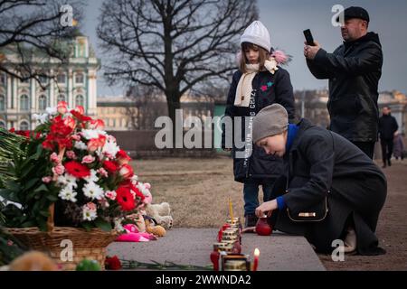 Eine Frau zündet Kerzen an einer spontanen Gedenkstätte für die Opfer des Terroranschlags im Rathaus von Crocus an, die auf der Nehrung der Insel Wassiljewski im Zentrum von St. Petersburg organisiert wurde. Russland betrauert die Opfer des Terroranschlags im Rathaus von Crocus in Moskau. Der 24. März wurde zum nationalen Trauertag im Land. Menschen in ganz Russland bringen Blumen zu spontanen Gedenkstätten, um Blumen zu legen und das Gedenken an die Opfer des Terroranschlags zu ehren. Nach den neuesten Daten des Untersuchungskomitees Russlands sind 137 Todesfälle bekannt, die Zahl könnte steigen. Trümmer sind immer noch vorhanden Stockfoto