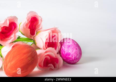Ostereier und rosa Rosenblüten auf weißem Hintergrund mit Platz für Text. Osterkonzept. Stockfoto