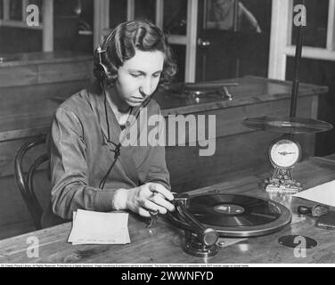 Grammophon-Schallplatten werden hergestellt und getestet 1941. Eine Frau, die Kopfhörer trug, sah, wie sie den Ton des RecordPlayers vor sich aufmerksam hörte. Es gibt auch eine Skala, auf der ein Datensatz platziert wird, um die Details des Gewichts zu kontrollieren, das ist richtig. Stockfoto