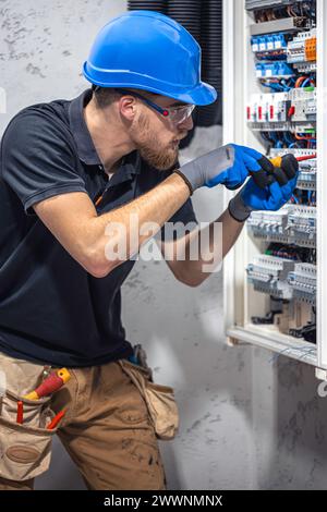 Ein Elektriker arbeitet in einer Schalttafel mit einem elektrischen Anschlusskabel. Stockfoto