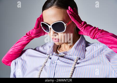 Elegante Frau mit Perlen und trendiger Sonnenbrille, mit pinkfarbenen Handschuhen und mit der Stirn Stockfoto