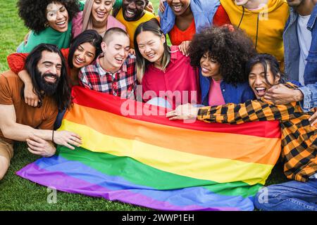 Verschiedene Menschen haben Spaß, die LGBT-Regenbogenfahne im Freien zu halten - multirassische Freunde, die nach dem Gay Pride Event Spaß haben - konzentrieren Sie sich auf die mittlere Glatze Stockfoto