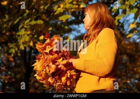 Herbstfrau mit trockenen Blättern. Freiwillige hacken und schnappen sich einen kleinen Haufen gelber, gefallener Blätter im Herbstpark. Den Rasen vom alten lea reinigen Stockfoto