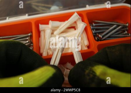 Auswahl der Dübel. Weiße Kunststoffdübel unterschiedlicher Größe in den Händen eines Baumeisters. Stockfoto