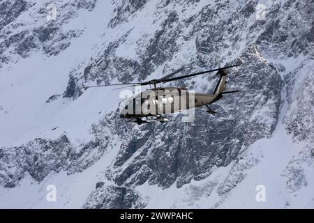 Ein Hubschrauber der Alaska Army National Guard UH-60L Black Hawk fliegt zwischen den Chugach Mountains und unterstützt dabei das Trainieren von Schleuderlasten in der Nähe der Joint Base Elmendorf-Richardson, Alaska, 28. Februar 2024. Soldaten der US-Armee des Alaska Army National Guard Aviation Battalion führten das mit Schleudern beladene Training durch, um ihre Einsatzfähigkeit in Alaskas rauer Umgebung zu verbessern. (Alaska Nationalgarde Stockfoto