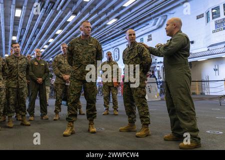 General David Camacho Jr., rechts, Leiter der Wartungskontrolle der Marine Medium Tiltrotor Squadron 265 (rein.), 31. Marine Expeditionary Unit, unterstützt Lance CPL. Ethan Tracy, zweiter von rechts, einen CH-53 Hubschraubermechaniker mit VMM-265 (rein.), 31. MEU, an Generalmajor Eric Austin, Zentrum, der kommandierende General des 1st Marine Aircraft Wing, III Marine Expeditionary Force, für Tracys überlegene Arbeit während der gesamten Patrouille an Bord des amphibischen Angriffsschiffs USS America (LHA 6) in der Philippinischen See, 13. Februar 2024. Austin leitete die Ausbildung und das Wohlergehen der Marines ab den 1ern Stockfoto