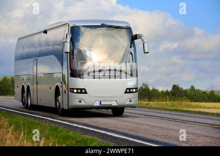 Silberner Reisebus, der im Spätsommer auf der Autobahn durch ländliche Landschaften fährt, blauer Himmel und Wolken im Hintergrund. Stockfoto