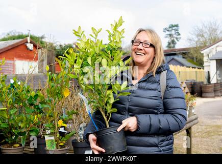 Eine ältere Frau lächelt, während sie an einem kalten Tag Pflanzen in einem Gartencenter-Laden kauft. Stockfoto