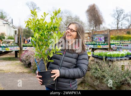 Eine ältere Frau lächelt, während sie an einem kalten Tag Pflanzen in einem Gartencenter-Laden kauft. Stockfoto