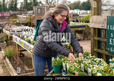 Eine ältere Frau lächelt, während sie an einem kalten Tag Pflanzen in einem Gartencenter-Laden kauft. Stockfoto