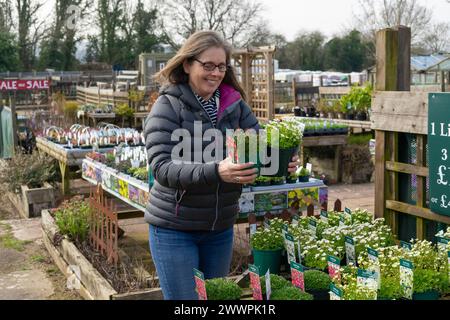 Eine ältere Frau lächelt, während sie an einem kalten Tag Pflanzen in einem Gartencenter-Laden kauft. Stockfoto