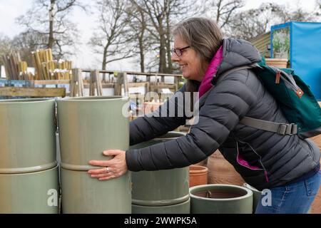 Eine ältere Frau lächelt, während sie an einem kalten Tag Pflanztöpfe in einem Gartencenter kauft. Stockfoto