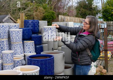 Eine ältere Frau lächelt, während sie an einem kalten Tag Pflanztöpfe in einem Gartencenter kauft. Stockfoto