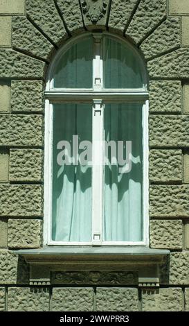 Ein antikes Zementblockgebäude in Osteuropa hat alte Holzrahmen Schlüssellochfenster, Gipsdekoration und Cherub um die Schwelle und das Gerüst. Stockfoto