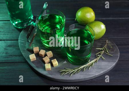 Absinth in Gläsern, Rosmarin, brauner Zucker und Limette auf Holztisch. Alkoholisches Getränk Stockfoto