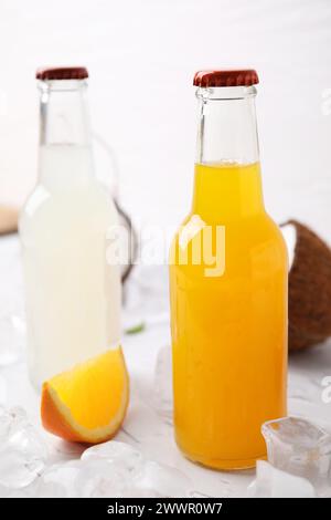 Leckere Kombucha in Glasflaschen, Orange und Eis auf weißem Tisch Stockfoto