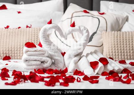 Flitterwochen. Schwäne mit Handtüchern und wunderschönen Rosenblättern auf dem Bett Stockfoto