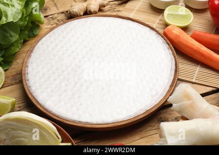 Köstliche Frühlingsbrötchen machen. Reispapier und andere Zutaten auf Holztisch, Nahaufnahme Stockfoto