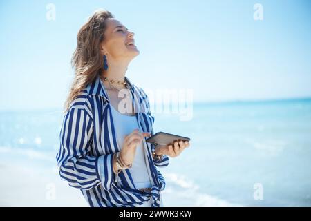 Glückliche elegante Frau mittleren Alters an der Küste mit Smartphone. Stockfoto