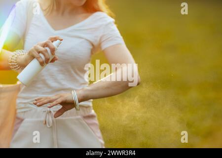 Sommerzeit. Nahaufnahme einer Frau in weißem Hemd, die Sonnencreme auf der Wiese im Freien aufträgt. Stockfoto