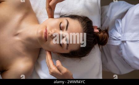 Kosmetologin-Hände, die einer Frau im Büro eine Gesichts- und Nackenmassage wegen Hautelastizität durchführen. Entspannte Kundin. Schönheitsbehandlung im Gesicht Stockfoto