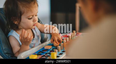 Kleines Mädchen, das im Haus am weißen Tisch mit Stapeln und Zählen spielt. Kinderspielzeug Stockfoto