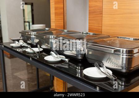 Reihe geschlossener Scheuerschalen im Festsaal. Marmites stehen für den Service bereit, hergestellt aus Edelstahl am Buffet. Stockfoto