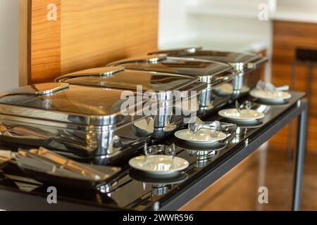 Reihe geschlossener Scheuerschalen im Festsaal. Marmites stehen für den Service bereit, hergestellt aus Edelstahl am Buffet. Stockfoto