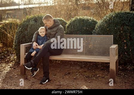 Herbstliche Familienzusammenhänge: Vater, 40 Jahre alt, und Sohn - wunderschöner 8-jähriger Junge, im Park sitzend. Stockfoto