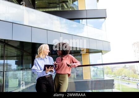 Zwei Frauen mit ähnlichen Merkmalen stehen nebeneinander, lächelnd, vor der großen Architektur. Stockfoto