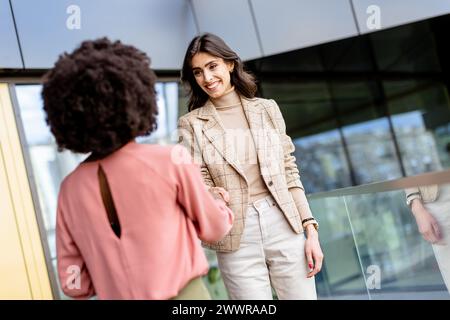 Zwei Frauen machen einen freundlichen Handschlag, eine lacht fröhlich und symbolisiert eine positive Geschäftsbeziehung. Stockfoto
