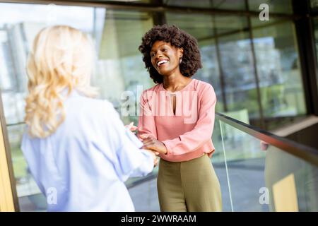Zwei Frauen machen einen freundlichen Handschlag, eine lacht fröhlich und symbolisiert eine positive Geschäftsbeziehung. Stockfoto