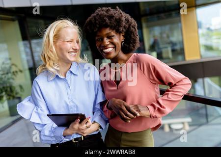 Zwei Frauen mit ähnlichen Merkmalen stehen nebeneinander, lächelnd, vor der großen Architektur. Stockfoto