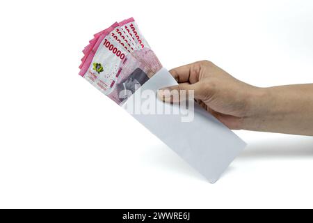 Die Hand des asiatischen Mannes, der einen weißen Umschlag mit 100.000 IDR-Bargeld hält. Indonesische Rupiah Stockfoto