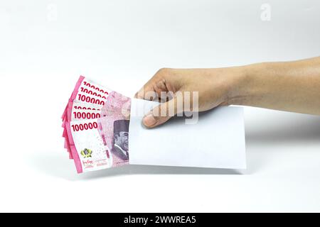 Die Hand des asiatischen Mannes, der einen weißen Umschlag mit 100.000 IDR-Bargeld hält. Indonesische Rupiah Stockfoto