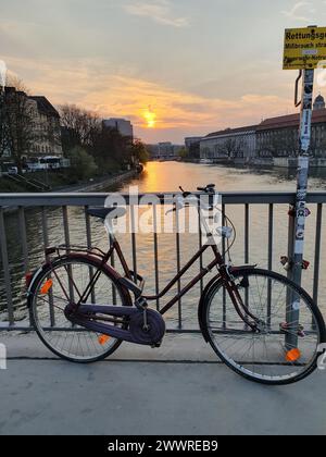 Ein Fahrrad, das sich während der Sonnenuntergangszeit am Zaun neben der Spree in Berlin, Deutschland, lehnt Stockfoto