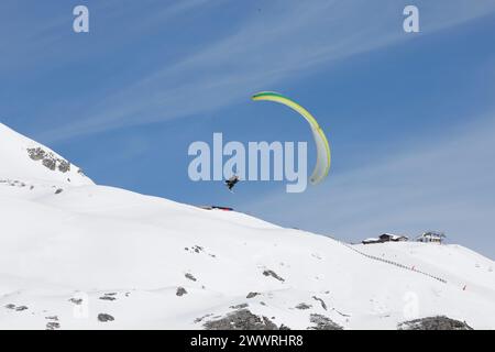 Ein Gleitschirmflieger auf Tandemflugplätzen über Schnee und Felsen in Tignes, einem hochgelegenen Skigebiet in den französischen Alpen. Stockfoto