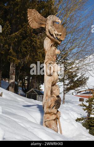 Ein hölzernes Totem mit jungen Bergsteigern, Mufflons, Eckzähnen und Adlern mit ausgespreizten Flügeln taucht aus dem Schnee am Seeufer in Tignes, Frankreich, hervor. Stockfoto