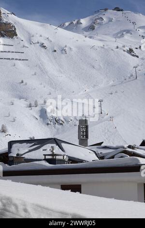 Der Glockenturm der modernistischen römisch-katholischen Kirche erhebt sich über schneebedeckten Dächern von Tignes, einem speziell erbauten Skigebiet in den französischen Alpen. Stockfoto