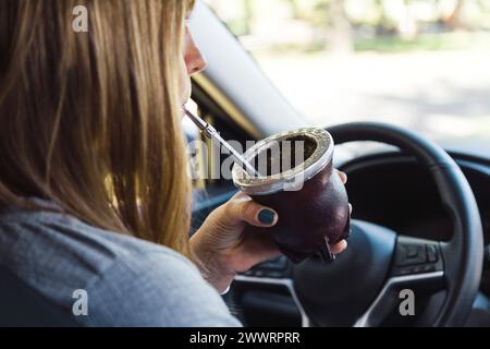 Blonde Frau mittleren Alters, die in einem Auto sitzt und Yerba-Mate-Infusion in einem Mate-Becher trinkt. Stockfoto