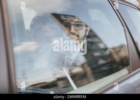 Besinnlicher junger Mann mit Brille, der durch ein Autofenster schaut Stockfoto