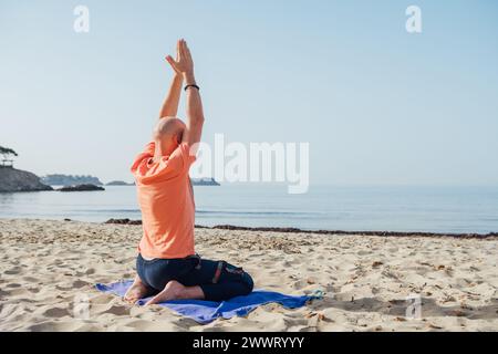 Ruhiger Mann, der in Seiza-Position sitzt, tiefe Atemübungen macht und in den frühen Morgenstunden am Sandstrand mit ruhigen Meereswellen meditiert. Menta Stockfoto