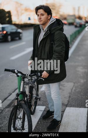 Lässig gekleideter junger Mann mit Fahrrad auf der Stadtstraße in der Abenddämmerung Stockfoto