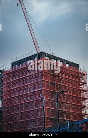 Baustelle mit einem hohen Gebäude mit rotem Gerüst und einem Kran gegen einen bewölkten Himmel in Leeds, Großbritannien. Stockfoto