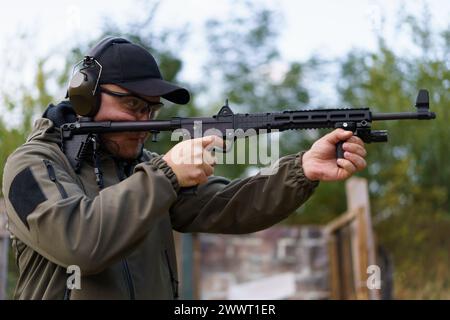 Ein Mann hält eine Waffe und trägt eine grüne Jacke. Er trägt einen schwarzen Hut und eine schwarze Brille Stockfoto