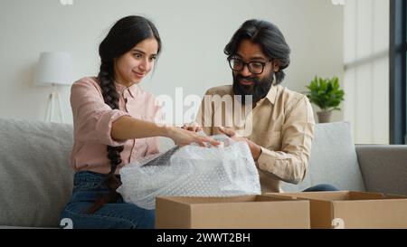 Aufgeregt verschiedene Kunden Paar öffnen Paket zu Hause glückliche Kunden arabische indische Frau Mann, die Bestellung online Shopping Store Lieferung auspackt Stockfoto